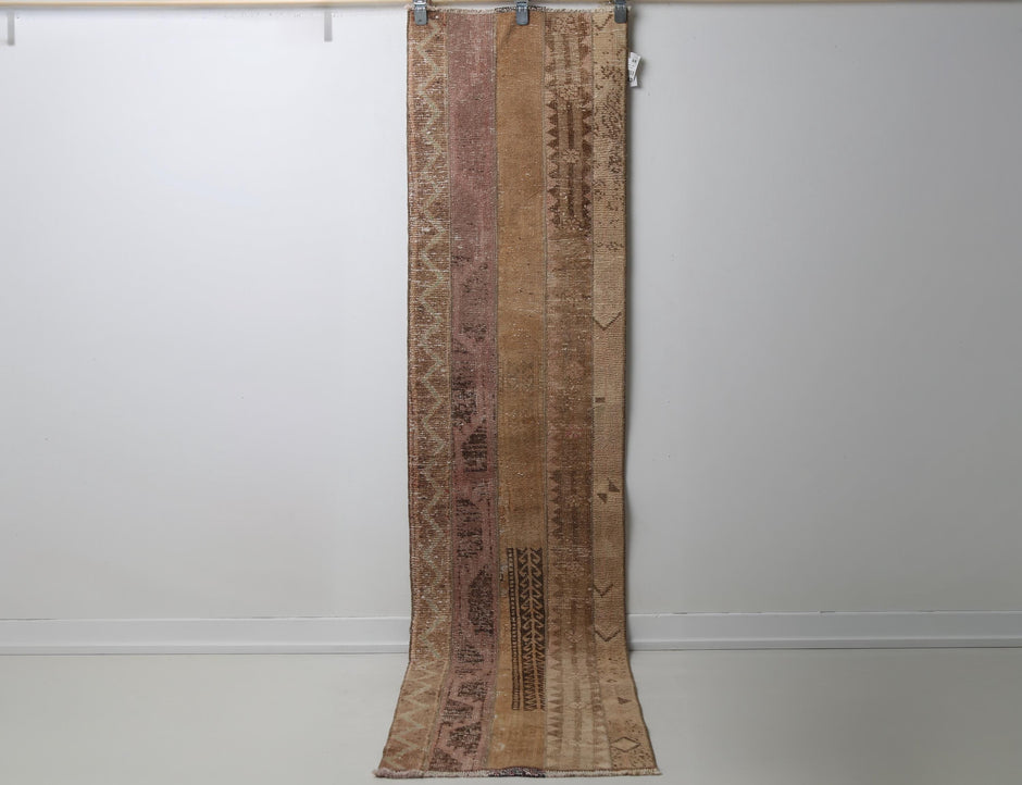 Vintage patchwork runner rug hanging showing brown and tan panel design
