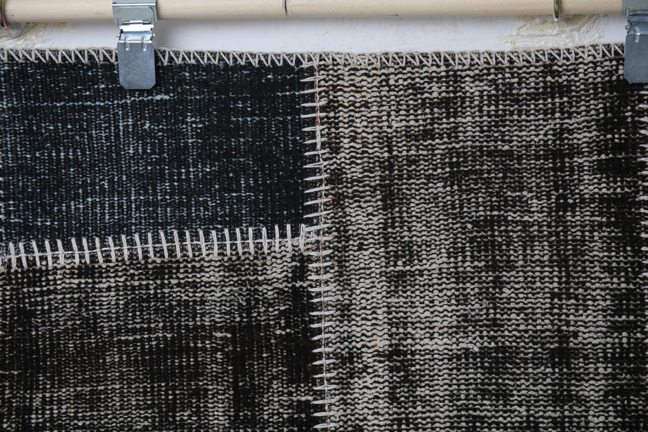 Close-up of handmade wool cotton rug showing dark charcoal distressed weave with white stitch trim