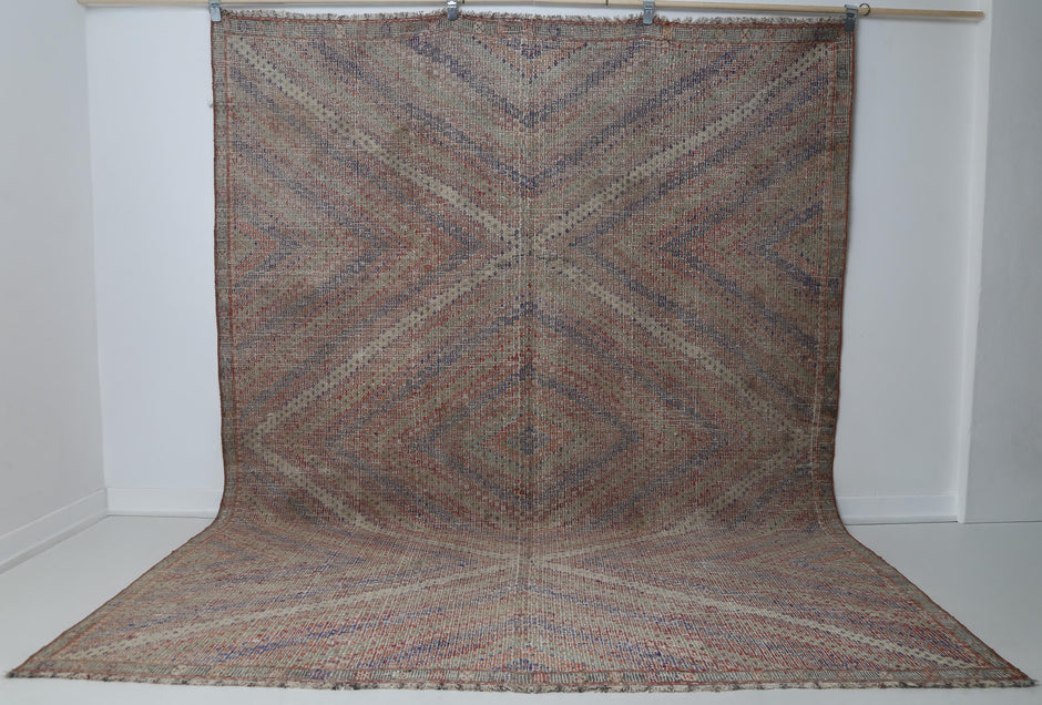 7x9 vintage Turkish kilim rug hanging showing full muted diagonal chevron pattern