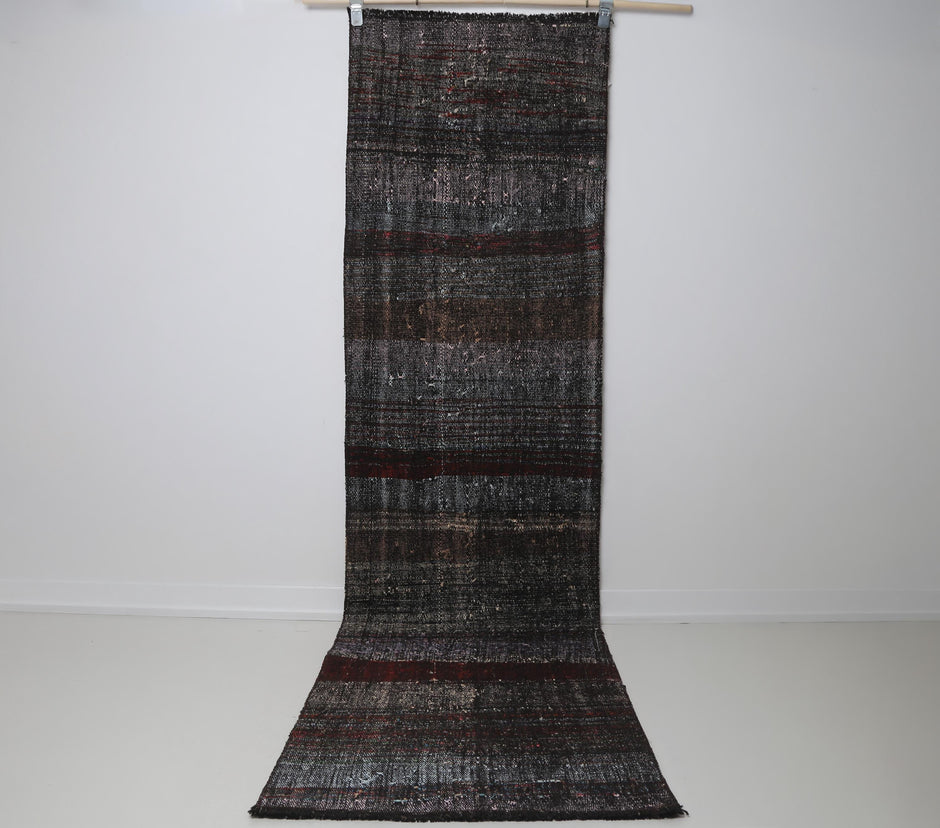 2x9 vintage Turkish flatweave runner rug hanging showing long black and red striped pattern