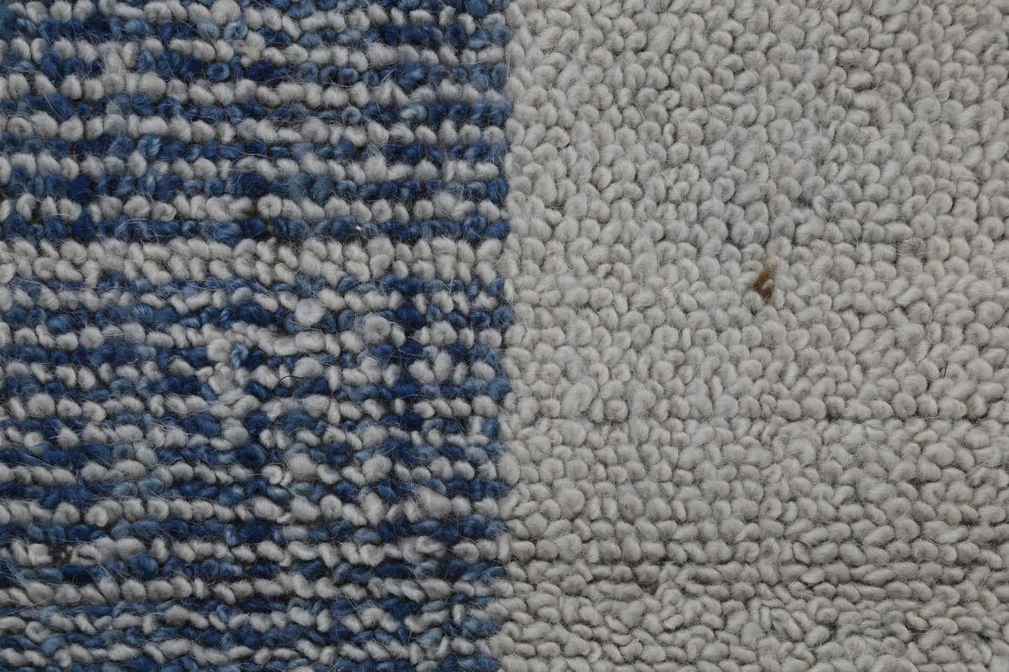 Close-up of a textured rug or carpet showing two distinct sections: a left side with a blue and white woven pattern, and a right side with a solid off-white bouclé texture.