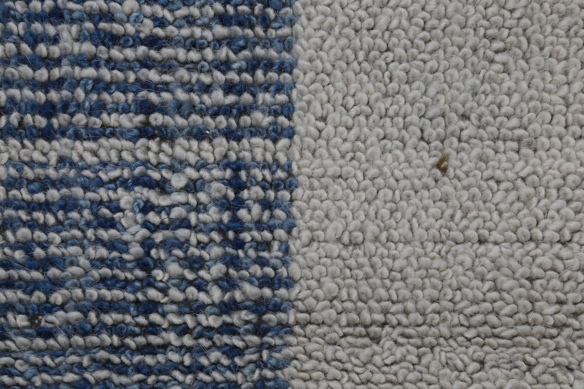 Close-up of a textured rug or carpet showing two distinct sections: a left side with a blue and white woven pattern, and a right side with a solid off-white bouclé texture.