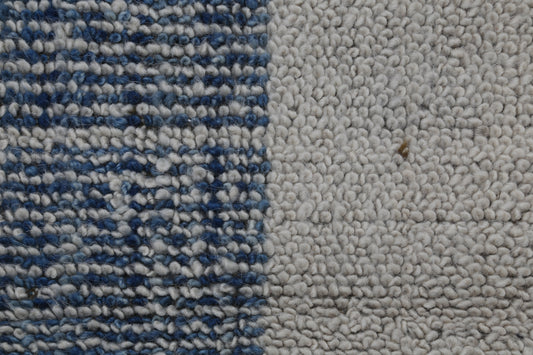 Close-up of a textured rug or carpet showing two distinct sections: a left side with a blue and white woven pattern, and a right side with a solid off-white bouclé texture.