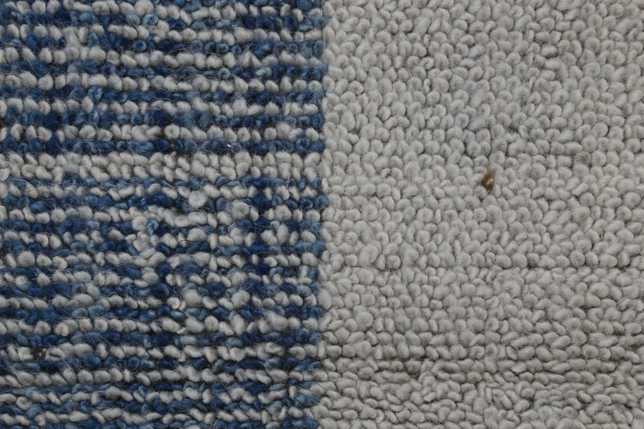 Close-up of a textured rug or carpet showing two distinct sections: a left side with a blue and white woven pattern, and a right side with a solid off-white bouclé texture.