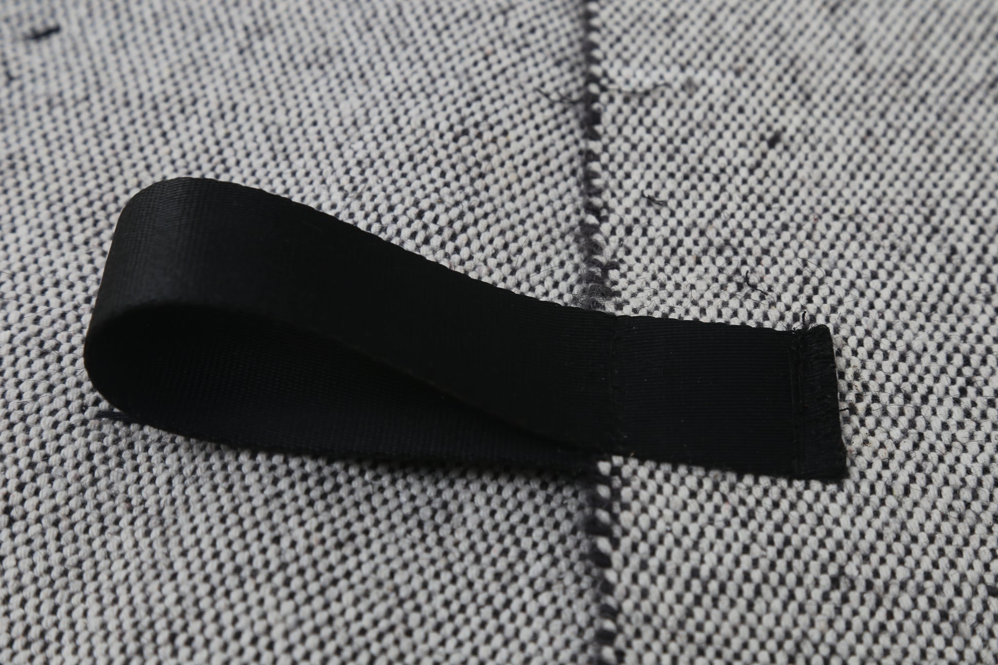 A black fabric loop or strap laid on a textured gray woven surface.