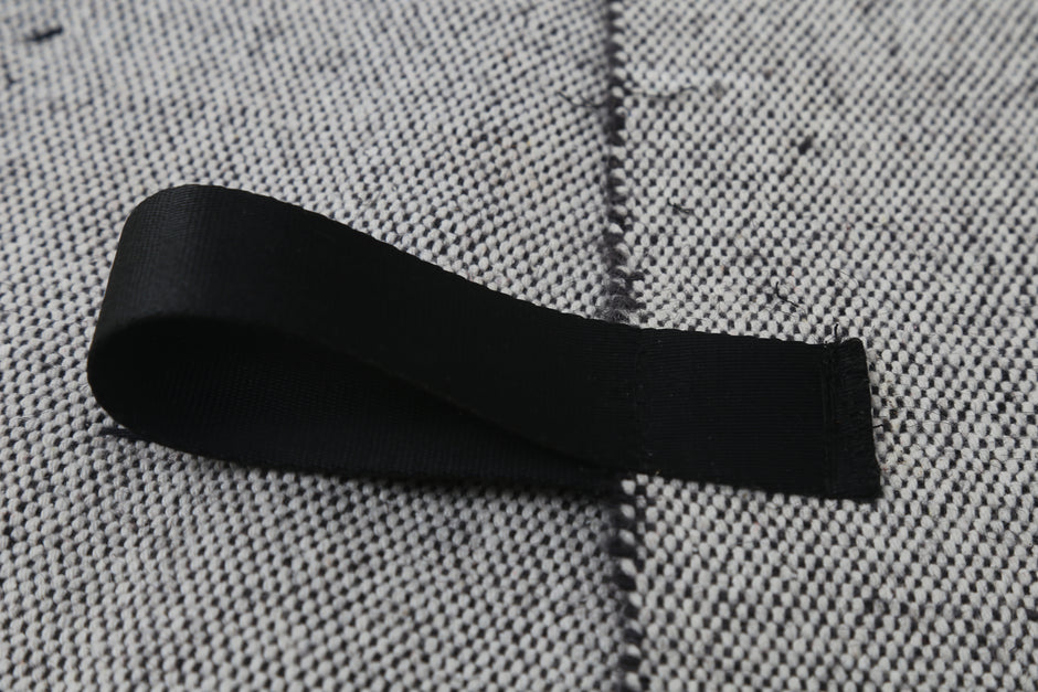 A black fabric loop or strap laid on a textured gray woven surface.