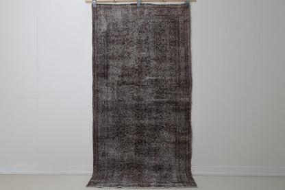 3'3 x 6'9 vintage Turkish rug hanging showing dark brown black distressed floral pattern