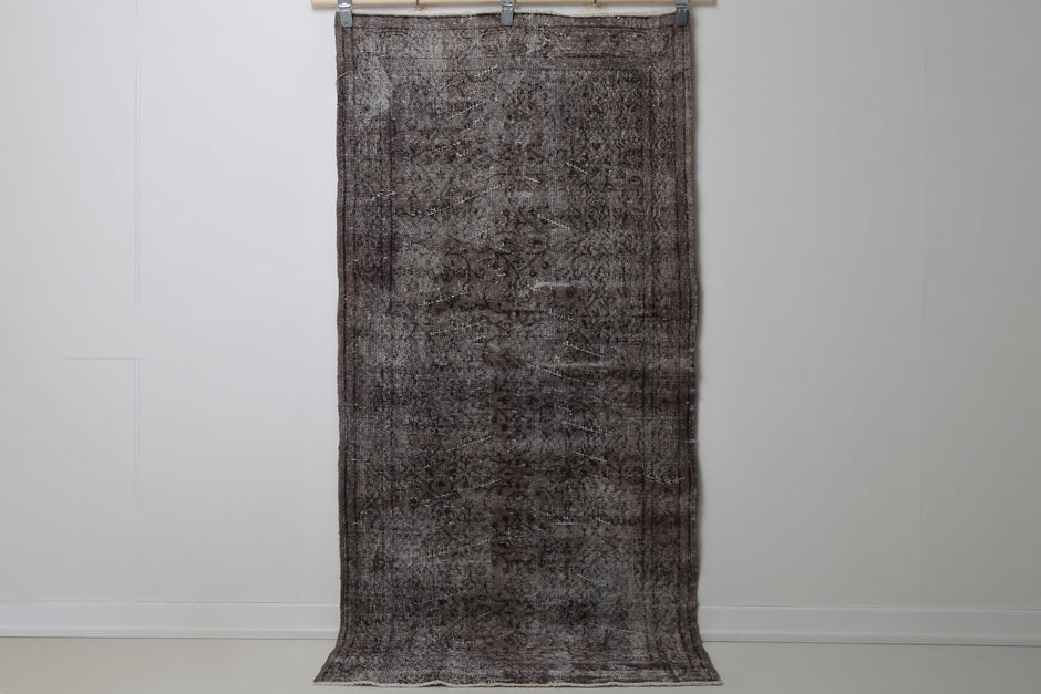 3'3 x 6'9 vintage Turkish rug hanging showing dark brown black distressed floral pattern