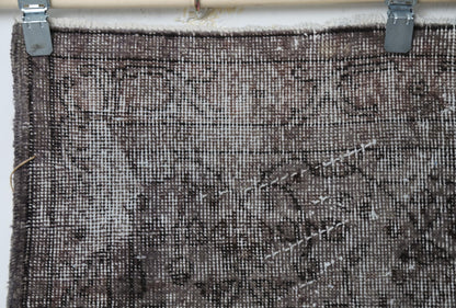 Full vintage Turkish rug hanging showing worn brown black floral area rug design