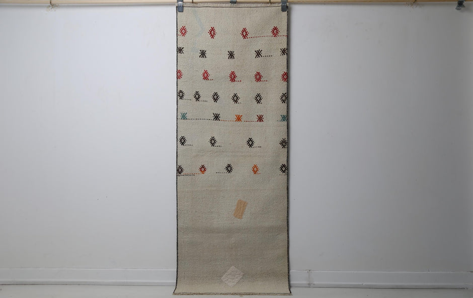 2'3 x 6'1 vintage Turkish kilim runner rug hanging showing beige field with scattered tribal diamond motifs