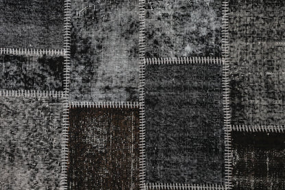 Full vintage patchwork rug hanging showing black brown mottled panels with white striped seams