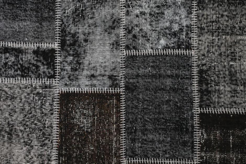 Full vintage patchwork rug hanging showing black brown mottled panels with white striped seams