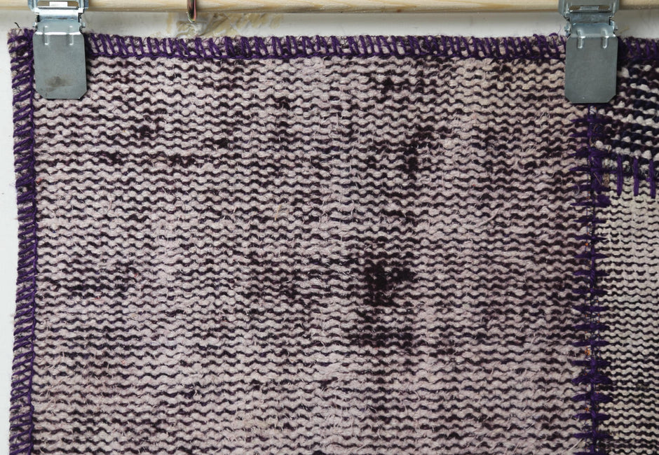 Close-up of vintage Turkish runner rug texture showing deep purple distressed woven panel