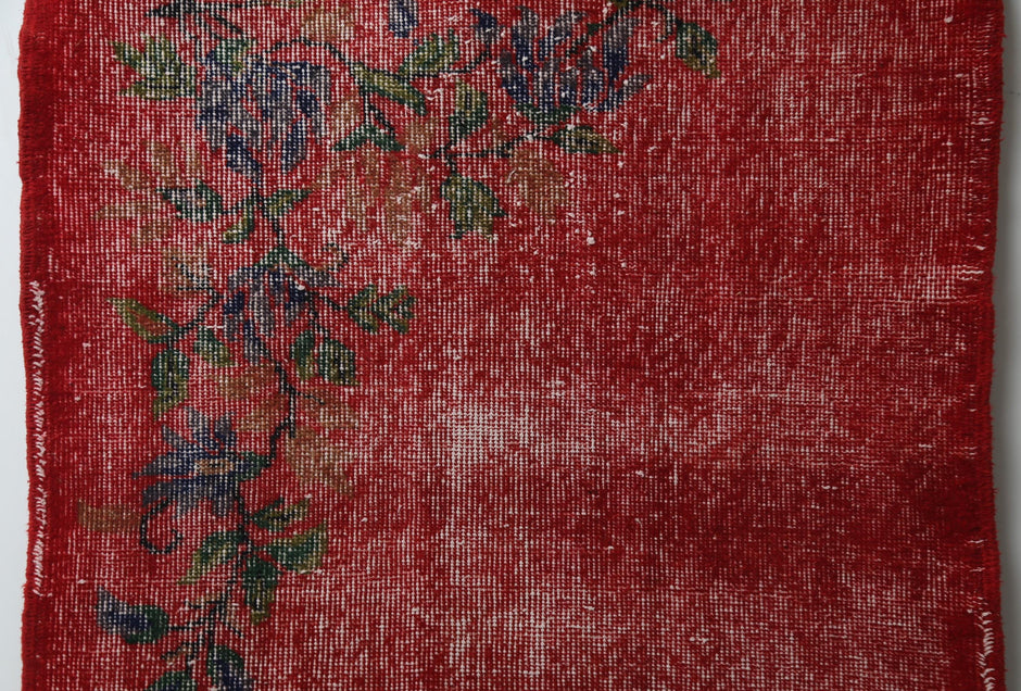 Detail shot of vintage Turkish runner rug texture showing faded red field with small floral accents
