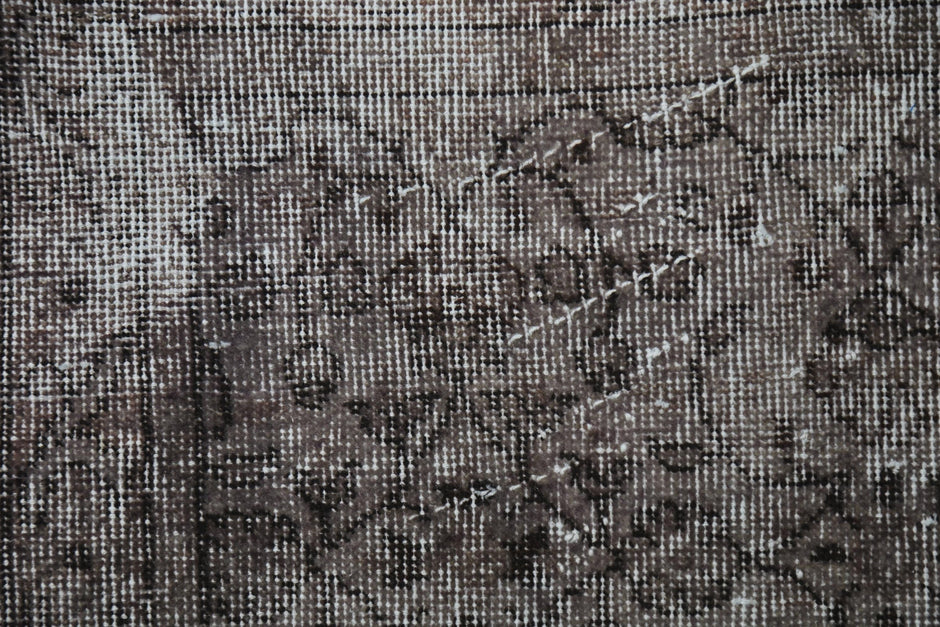 Detail shot of vintage Turkish rug texture showing faint floral pattern on charcoal brown field
