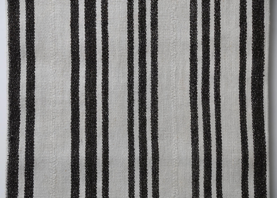 Detail shot of vintage Turkish runner rug texture showing black vertical stripe pattern on white fabric