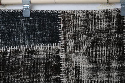 Close-up of handmade wool cotton rug showing dark charcoal distressed weave with white stitch trim
