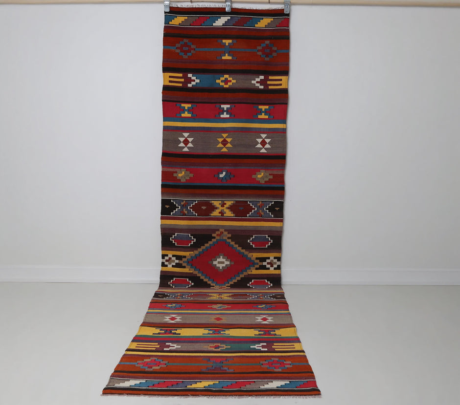 2'6 x 10'3 vintage Turkish kilim runner hanging showing long red tribal striped pattern