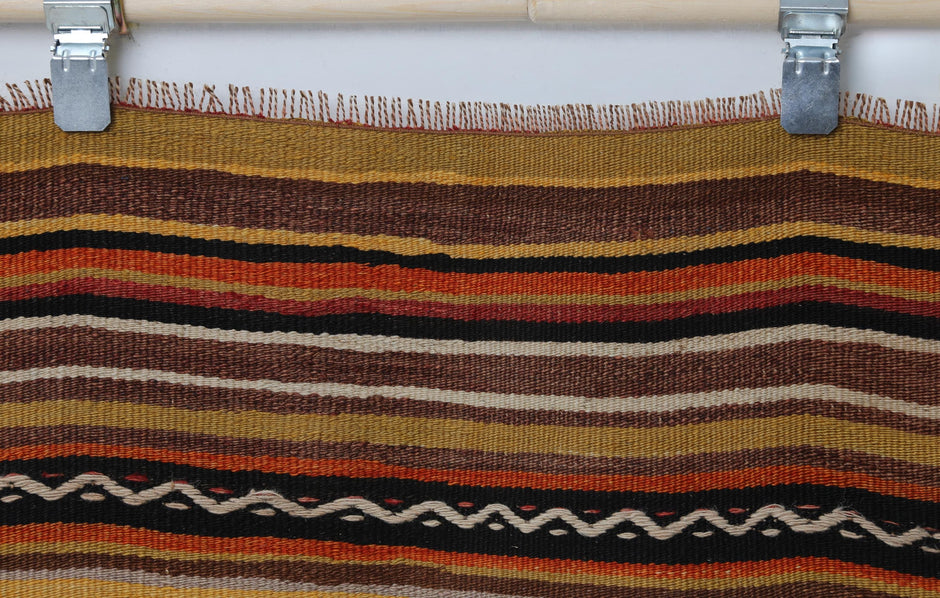 Detail shot of vintage Turkish rug texture showing gold, orange and black striped border pattern