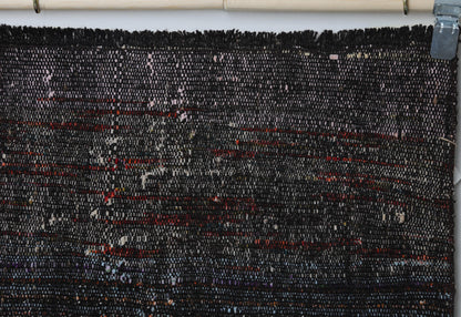 Close-up of handmade wool cotton runner rug showing black weave with subtle red stripe accents