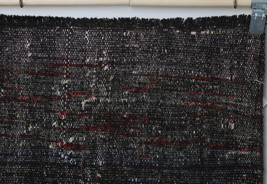 Close-up of handmade wool cotton runner rug showing black weave with subtle red stripe accents