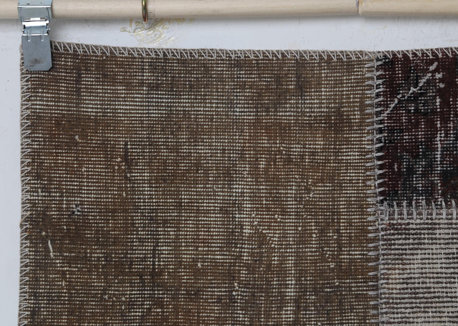 Full vintage patchwork runner rug hanging showing multicolor panels in brown, cream and dark tones