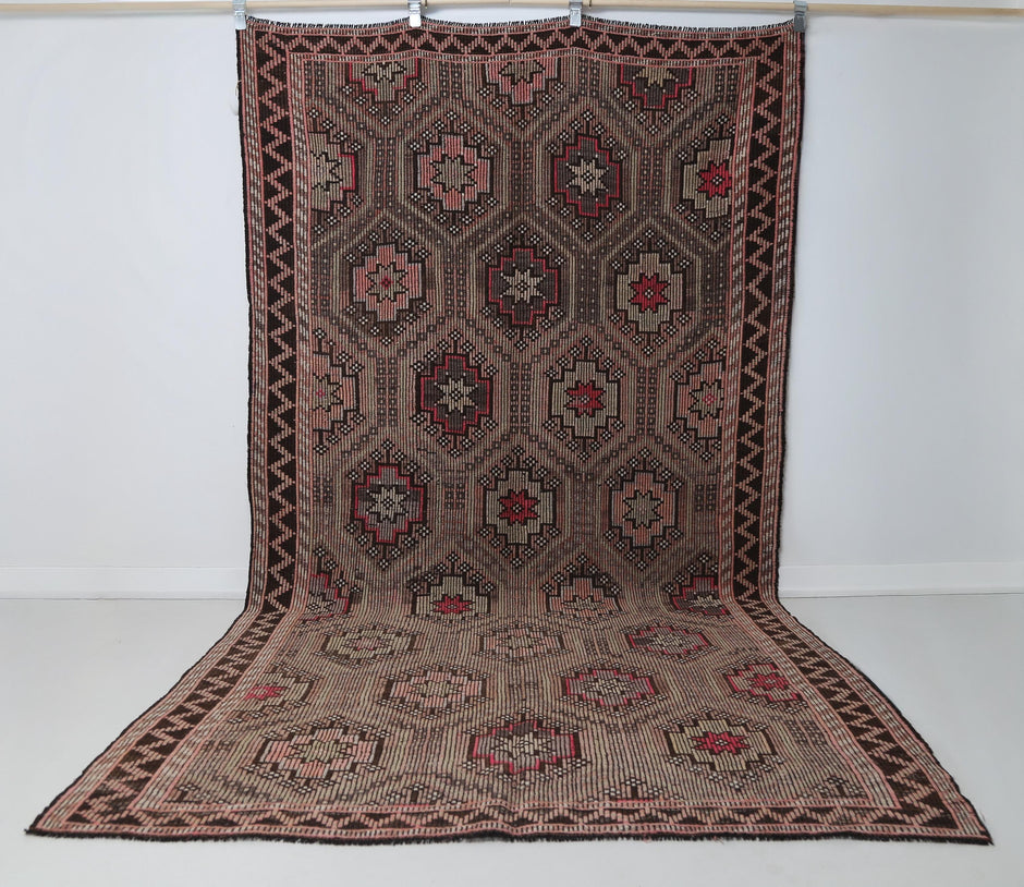 6x10 vintage Turkish kilim rug hanging showing full brown pink oriental geometric pattern