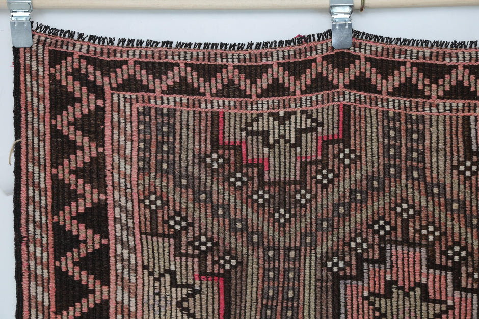 Close-up of vintage Turkish kilim rug showing pink diamond medallions on brown background