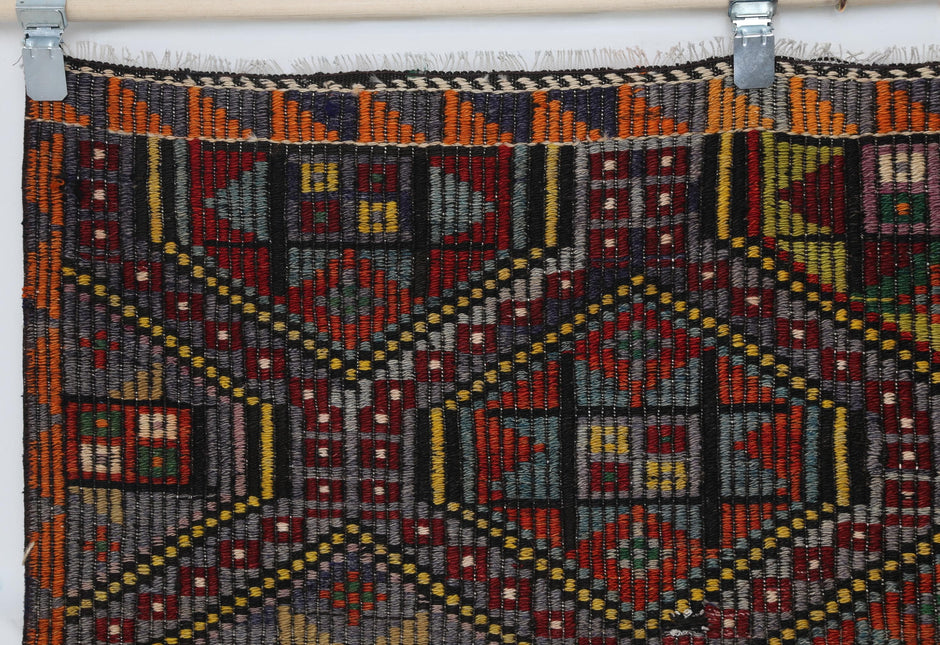 Close-up of vintage Turkish kilim rug corner showing red, orange, green and yellow tribal motifs