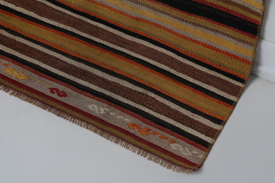 Full vintage Turkish kilim rug hanging showing multicolor horizontal stripes in warm earth tones