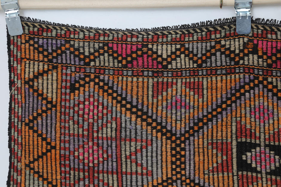 Detail shot of vintage Turkish rug weave showing red and orange geometric lattice with black accents