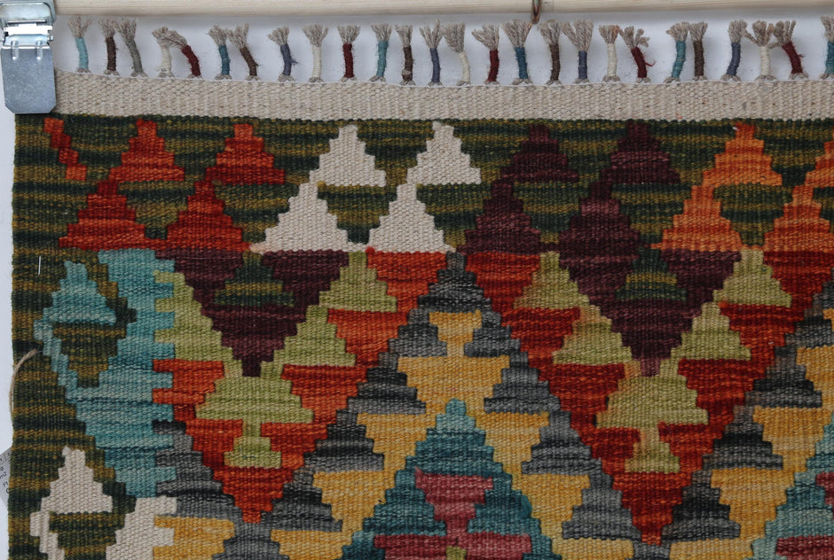 Full vintage Turkish kilim rug hanging showing dense multicolor geometric diamond and triangle design