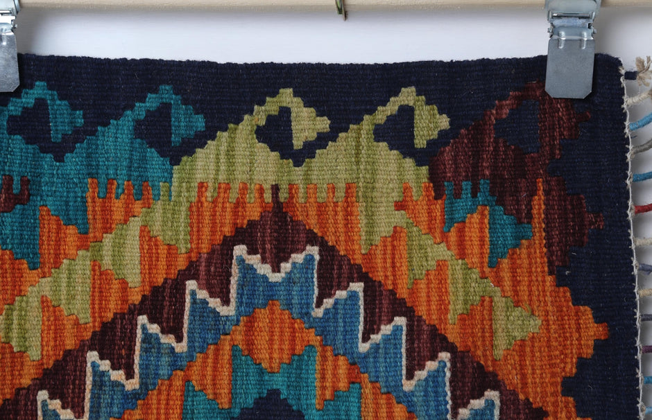 Close-up of handmade wool kilim rug showing orange and olive zigzag weave with blue accents