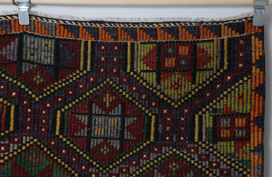 Close-up of handmade wool kilim rug showing dense tribal patterns in red, green and gold